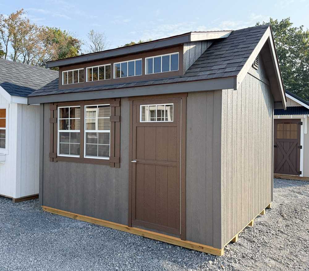Brown and tan garden shed from Salem Structures featuring transom windows, craftsman trim, single entry door, and upgraded roofline on gravel display lot.